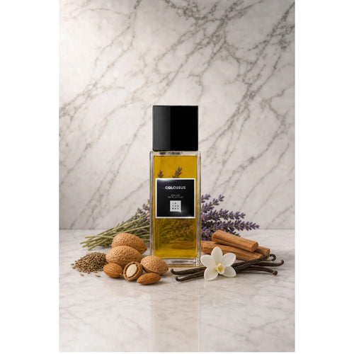 Frasco retangular do perfume Colossus In The Box, com líquido âmbar, tampa preta e rótulo escuro, sobre superfície clara com fundo de mármore. Ao redor, amêndoas, lavanda, baunilha e madeira.