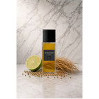 Frasco retangular do perfume Eau De Sauvery In The Box, com líquido âmbar, tampa preta e rótulo escuro, sobre superfície clara com fundo de mármore. Ao redor, limão verde, raízes e grãos claros.