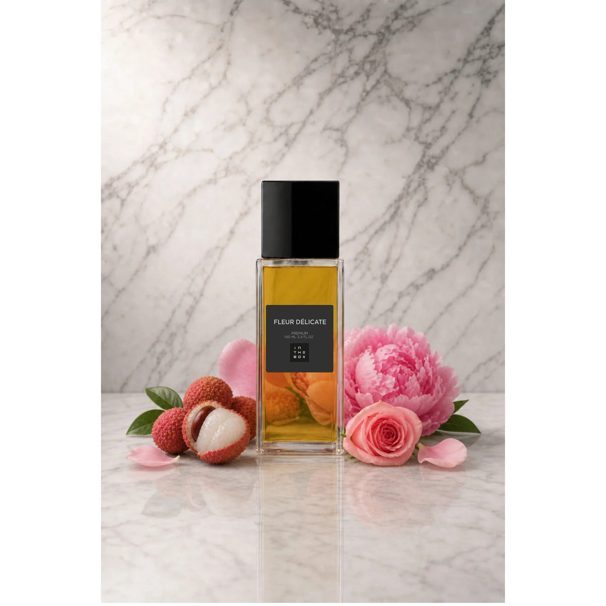 Frasco retangular do perfume Fleur Delicate In The Box, com líquido âmbar, tampa preta e rótulo escuro, sobre superfície clara com fundo de mármore. Ao redor, lichia, rosas e pétalas cor-de-rosa.